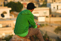 a man listening with earbuds sitting on a rock on a mountain 