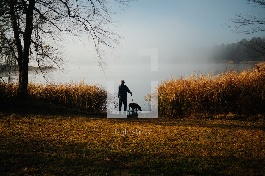man walking a dog by a misty lake 
