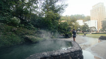 a woman standing near a steaming reflection pool 