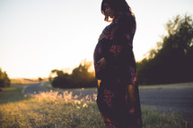 a pregnant woman standing outdoors holding her belly 