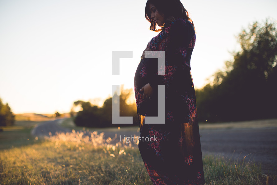 a pregnant woman standing outdoors holding her belly 