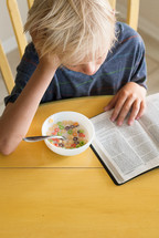 morning devotional, boy child reading a Bible while eating milk and cereal 
