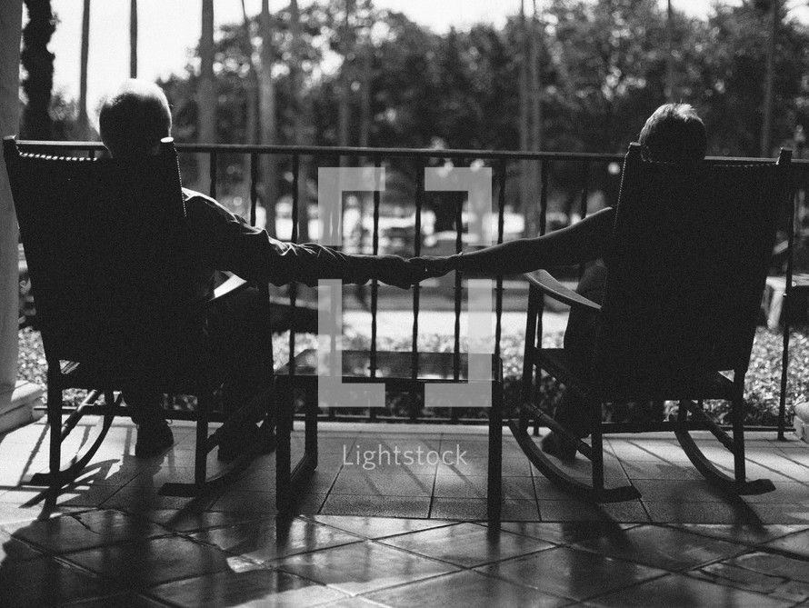 couple in rocking chairs holding hands on a porch