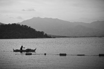 Man canoeing on open lake with mountain backdrop 
