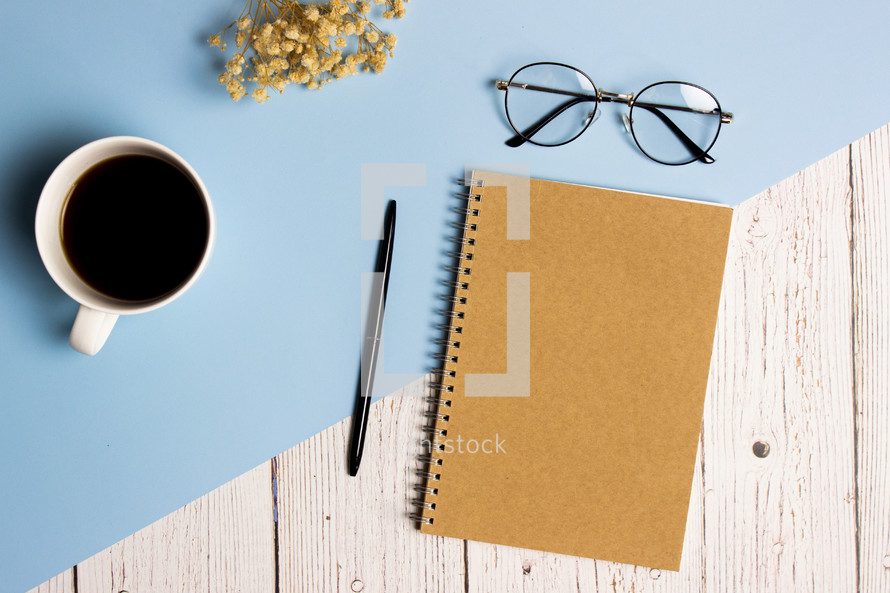 Writing concept with brown notebook, coffee cup, glasses and flowers over blue and wooden background. 