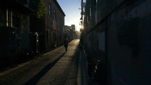 A woman walking through a downtown alley at sunset