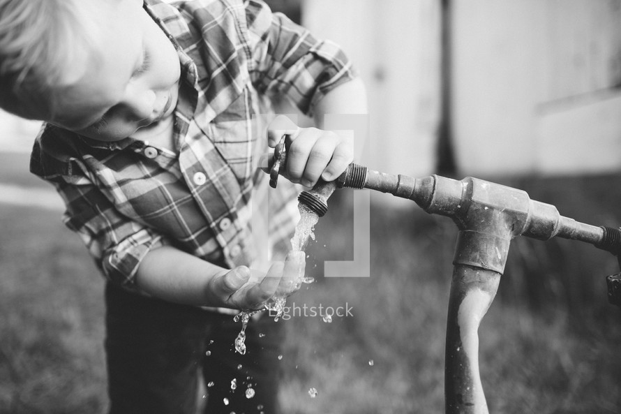 toddler boy washing his hands with an outdoor spigot