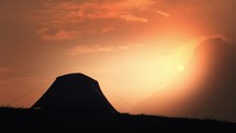 Silhouette of a male hiker climbing out of his tent on top of a mountain during sunrise