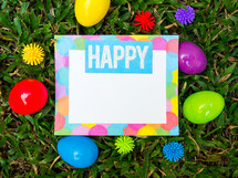 A colorful piece of paper and Easter eggs in green grass.