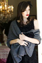 A young woman in a black dress wrapped in a shawl and leaning against a doorjamb vail model fashion
