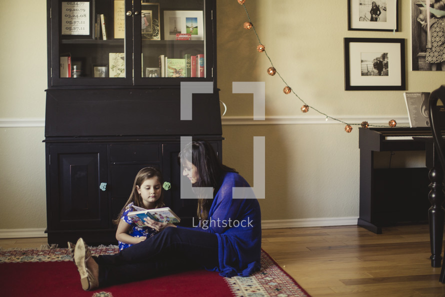 mother and daughter reading together sitting on a rug
