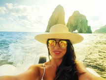 Happy woman takes a selfie on the boat near the Faraglioni of Capri island, Italy.