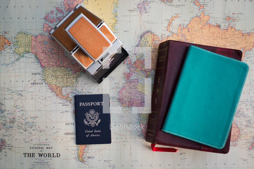 A passport, bible, notebook and a polaroid camera over an old world map.