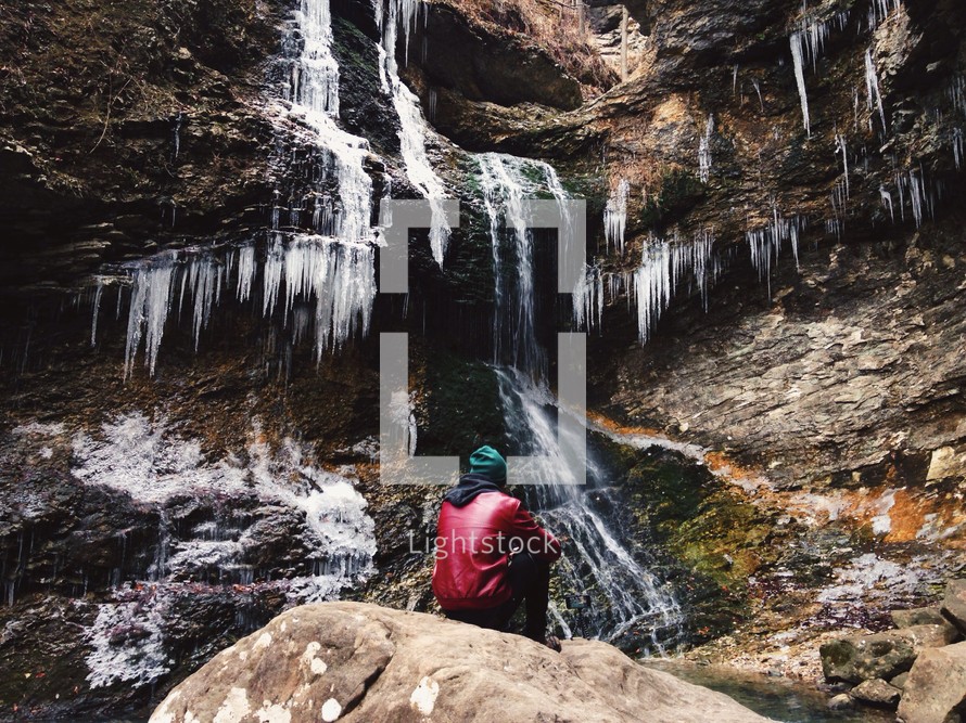A man sitting next to a frozen waterfall. 