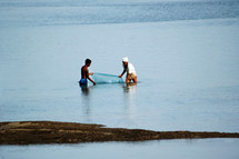 men in the ocean catching fish with a net 