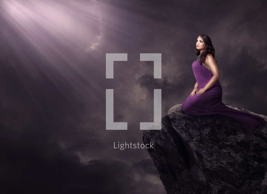 light shining on a woman on a rock in a purple dress 