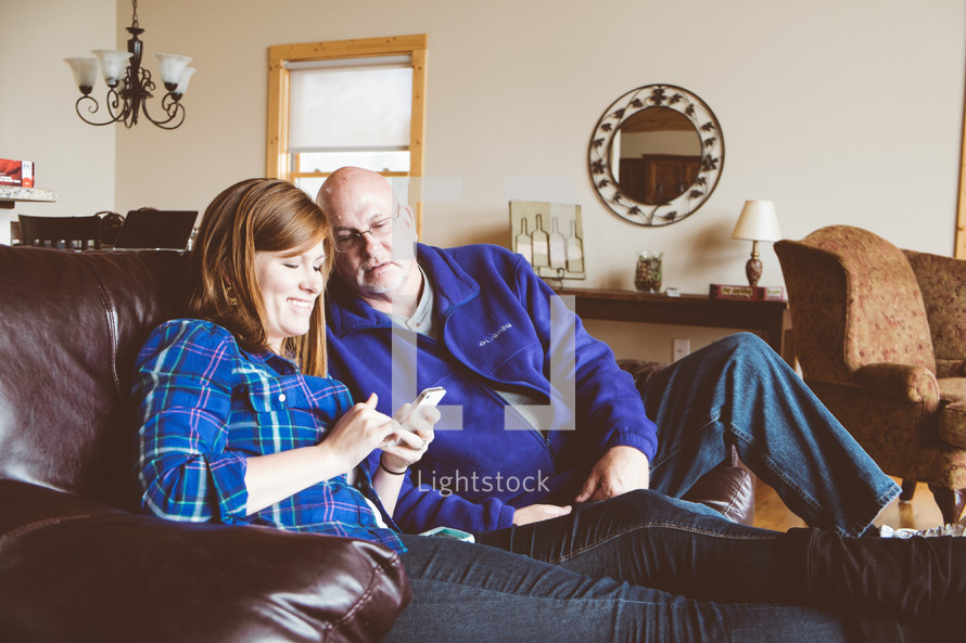 Couple sitting on a sofa looking at a cell phone.