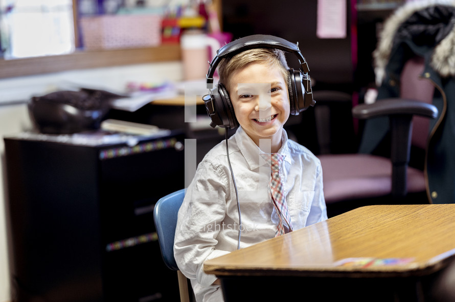 a boy sitting at a desk in a classroom wearing headphones 