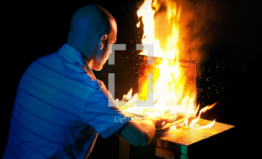man looking at a computer screen that is on fire 