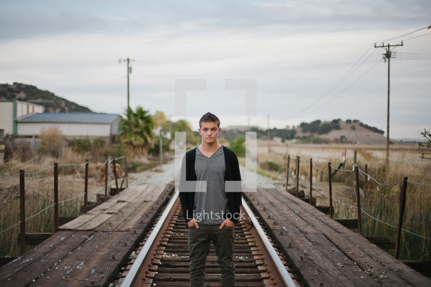 young man with hands in his pockets standing on railroad tracks