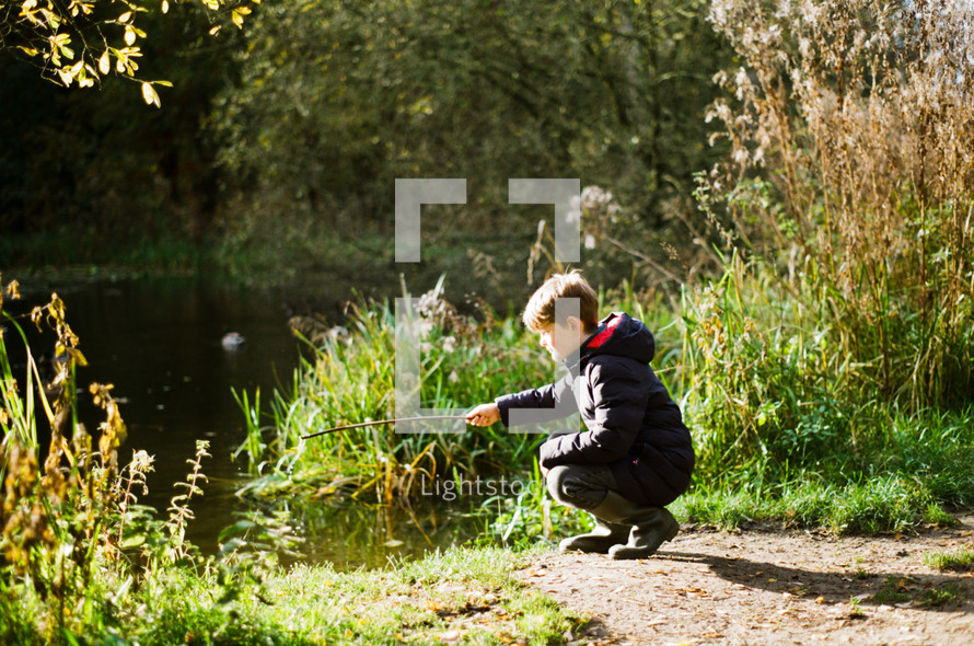 a boy playing with a stick near a pond 