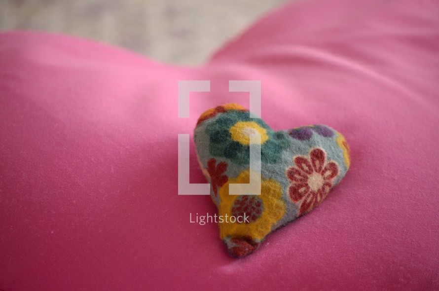 Small heart pillow with colorful flowers on a large pink heart pillow.