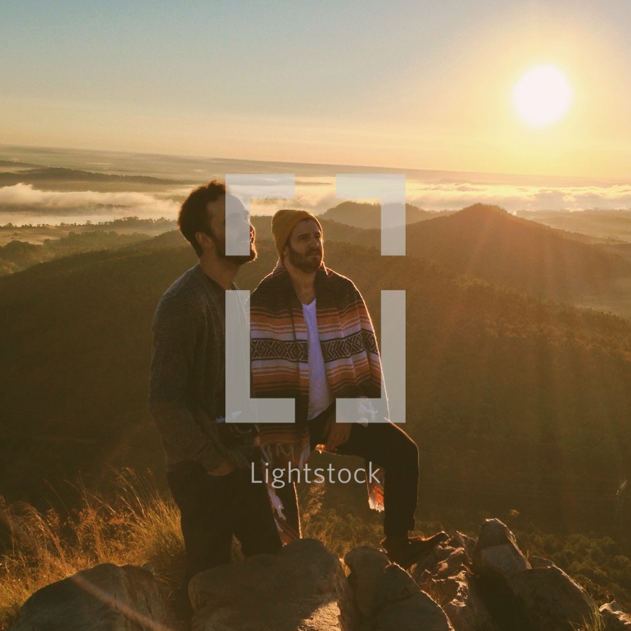 two men standing on top of a mountain under sunlight