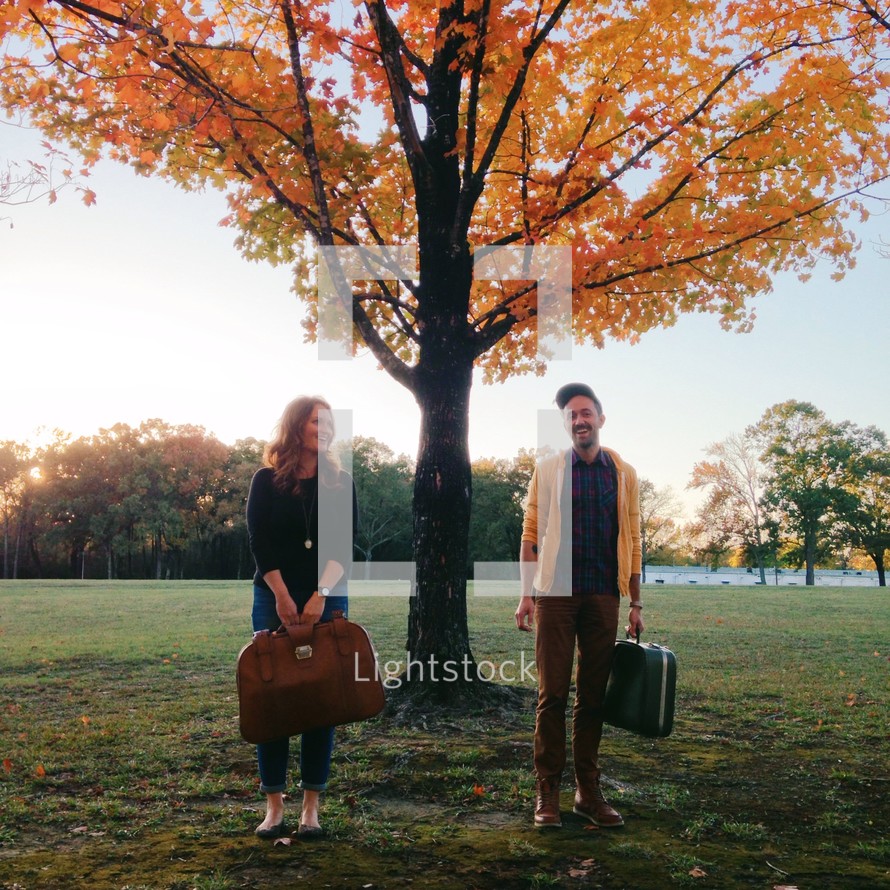 Couple carrying luggage through the park with fall foliage.