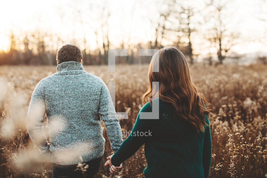 a couple holding hands walking through a field 