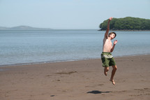 teen boy jumping for joy on a beach 