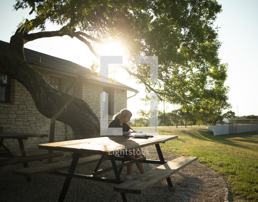 teen girl sitting at a picnic table reading a Bible 