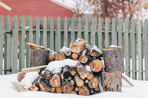 snow and axes near stack of firewood 