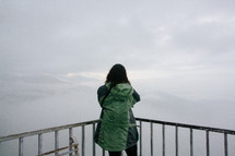 a woman looking out over a railing at mountains in the distance 