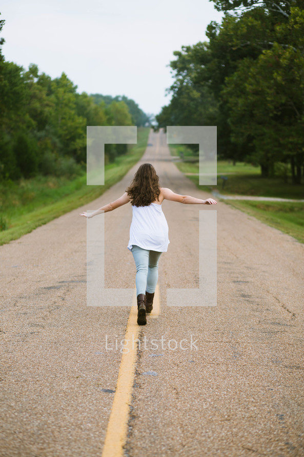 woman walking down the center lines of a rural road 
