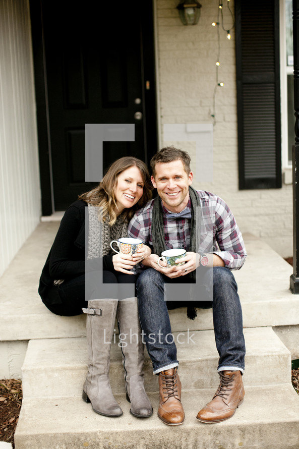 couple sitting on a step holding coffee 