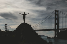  a person standing with outstretched arms and Golden Gate bridge in the background 
