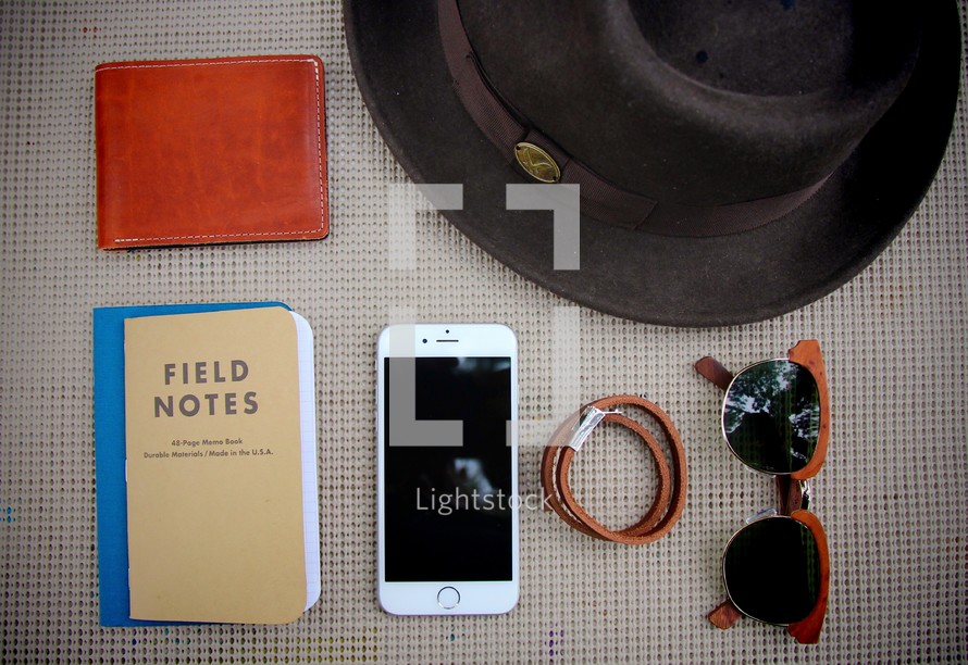 field notes, wallet, cellphone, sunglasses, hat, and hair ties on a table 