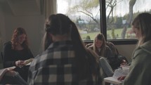 A small group of young adult women reading and discussing the Bible in a room with windows and natural light.
