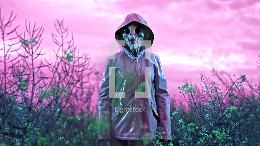 Portrait of spooky alien in field under colorful neon light. Scary mask, vinyl smooth raincoat. UFO, extraterrestrial life, halloween cosplay concept. High quality photo