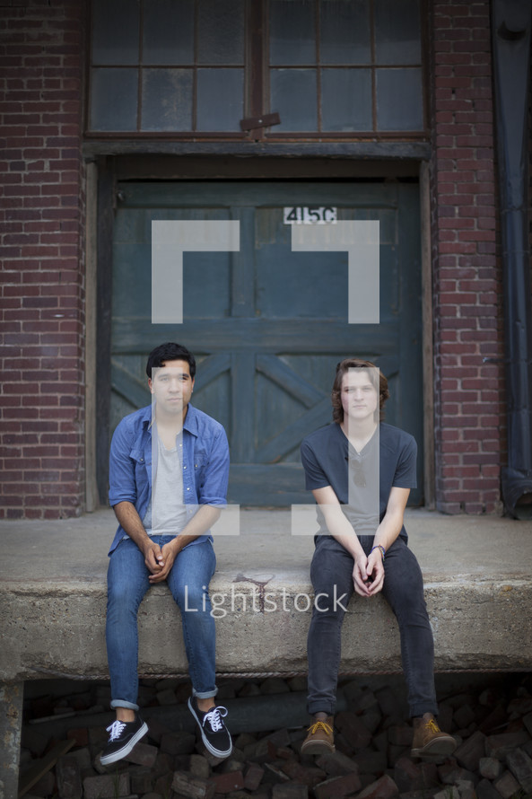 Two men sitting on a stoop in front of a warehouse 