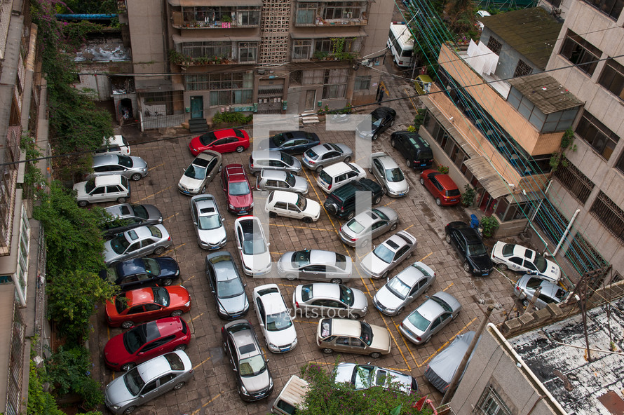 Cars parked in a lot in between apartment buildings.