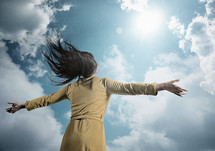 a woman with open arms standing under a blue cloudy sky 
