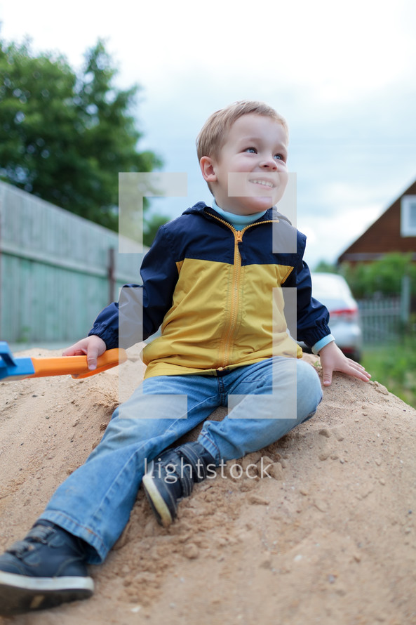 Happy little boy sitting on sand hill