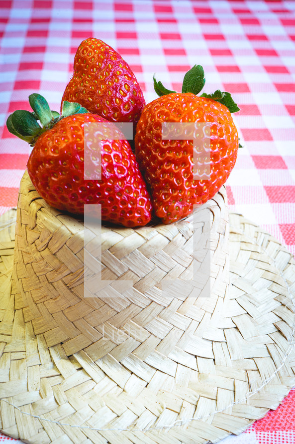 Fresh strawberries decorated on a straw hat. on a red picnic blanket.