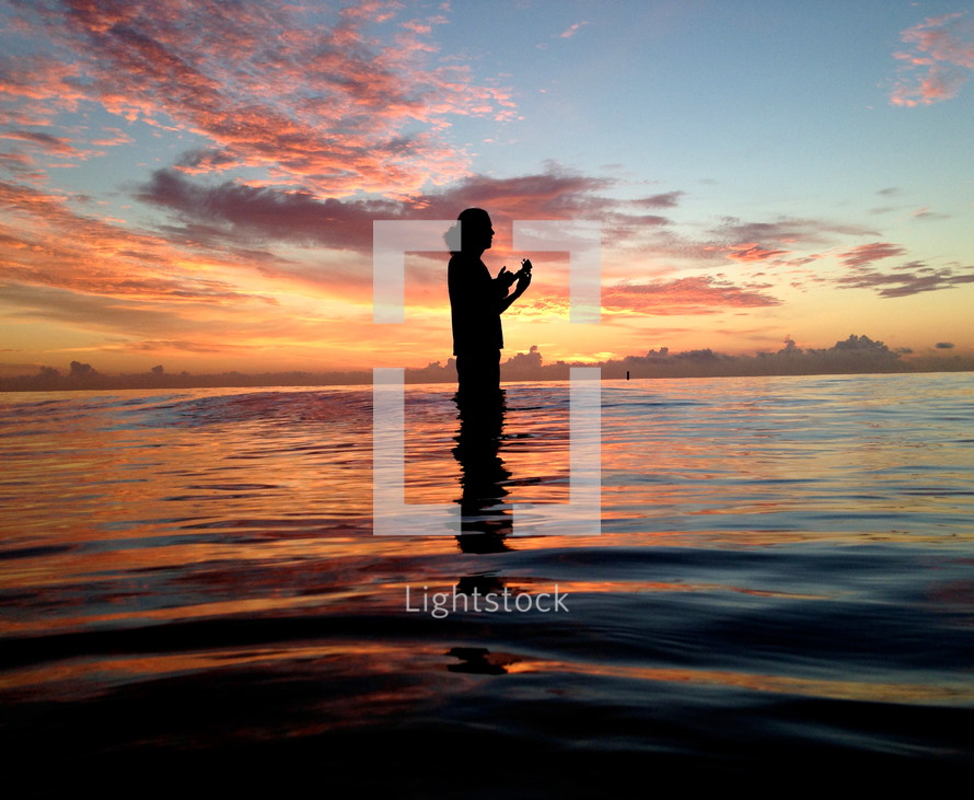 silhouette of a woman standing in water at sunset 