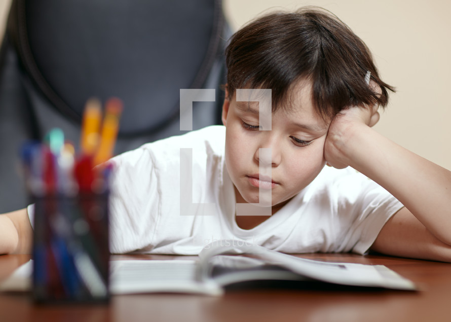 School boy studies hard over his book at home