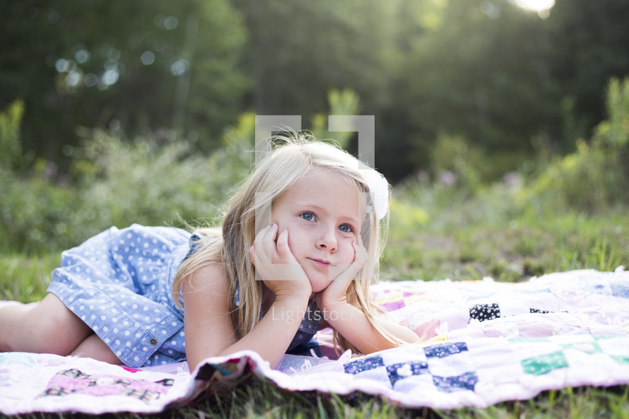 girl child lying on a blanket in the grass