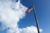 American flag on a tall flag pole against a blue sky.