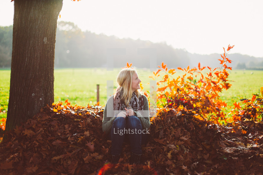 woman sitting in a pile of fall leaves outdoors 