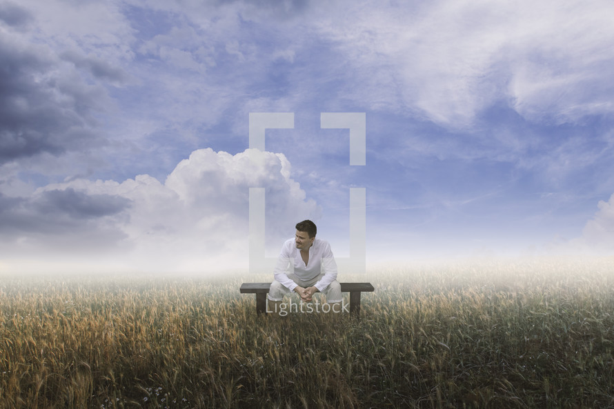 a man sitting in a field under a blue sky 